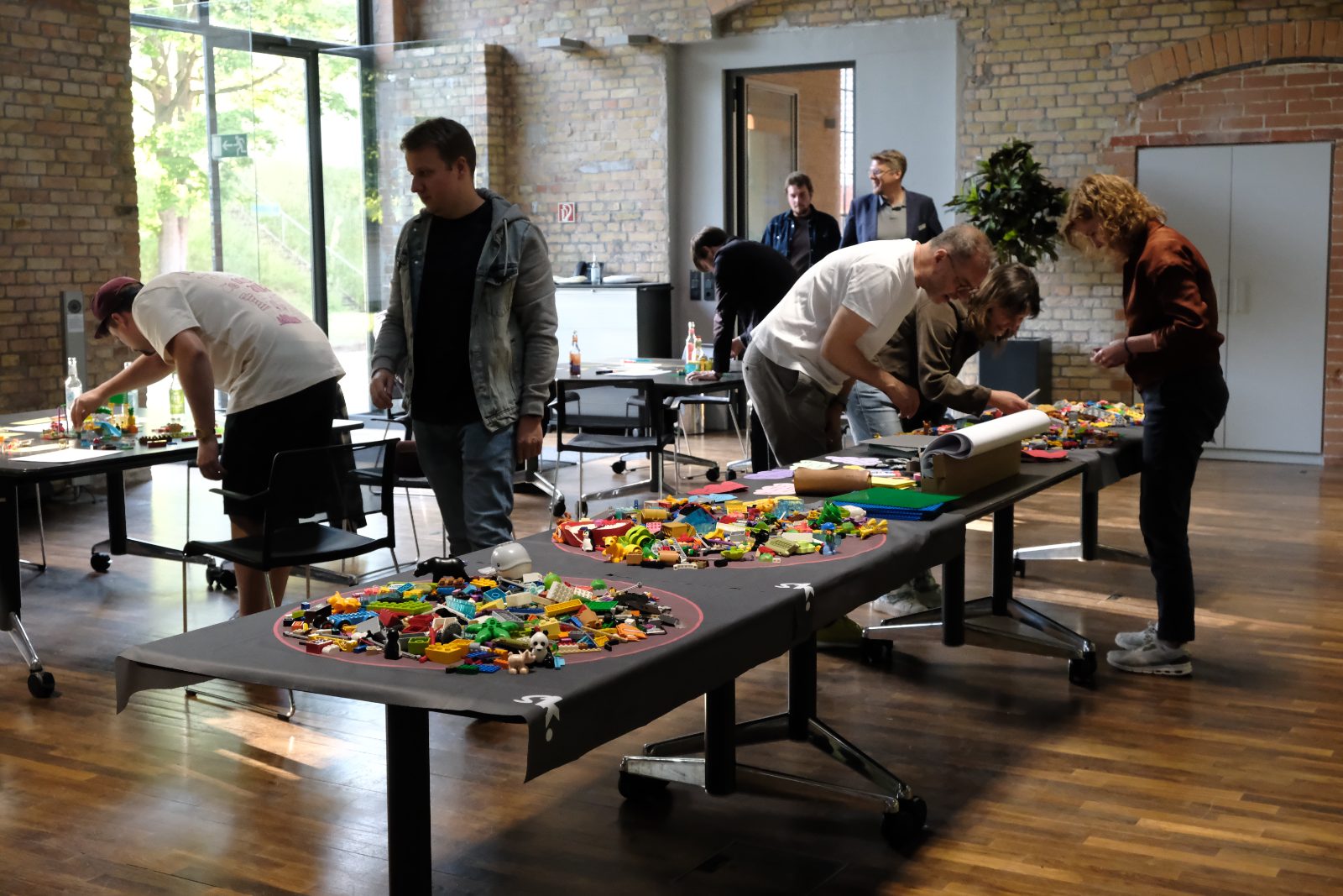 Workshop-Szene mit mehreren Teams an LEGO® SERIOUS PLAY® Tischen in einem hellen Raum